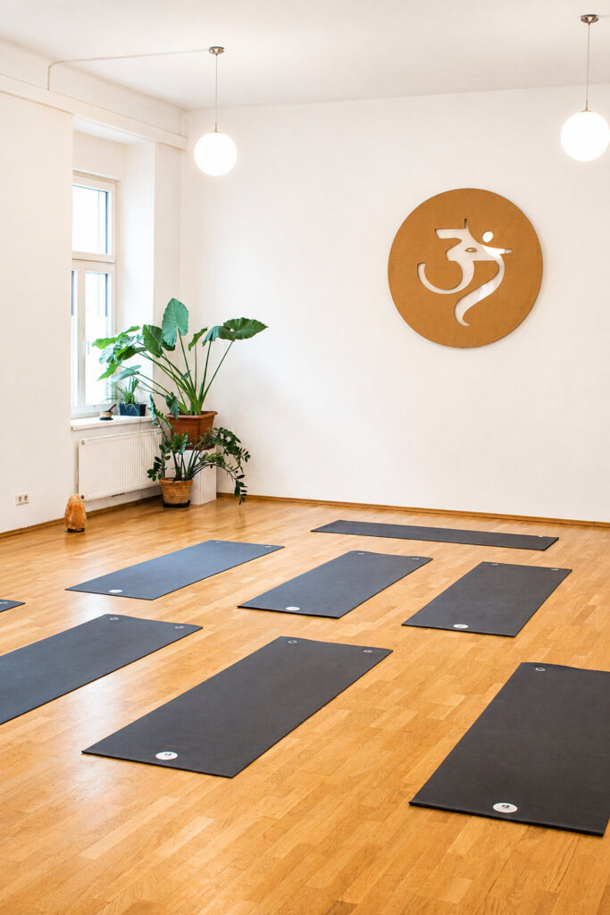 Heller Yogaraum mit Holzboden, Yogamatten und Om-Symbol an der Wand